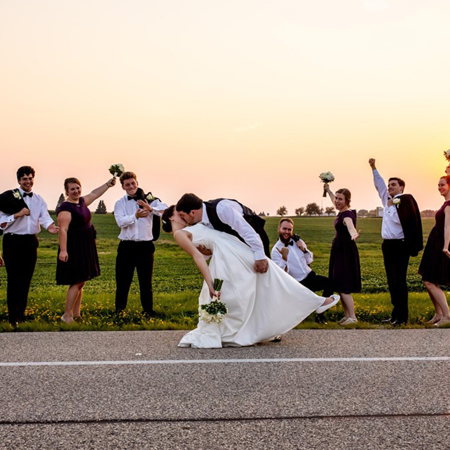 Bride and Groom kiss with bridesmaids and groomsmen outside the rochester event center during a beautiful sunset in Rochester Minnesota after the wedding